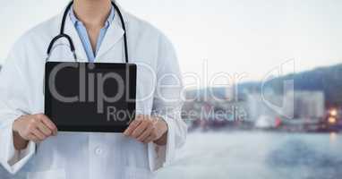 Doctor mid section with tablet against blurry skyline