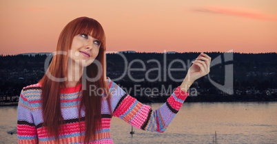 Redhead woman with arm raised looking up against lake