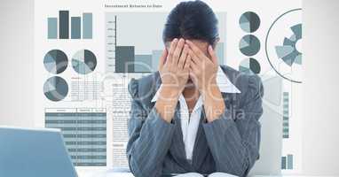 Stressed businesswoman sitting at desk against graphs