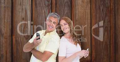 Smiling man and woman with smart phones over wooden wall