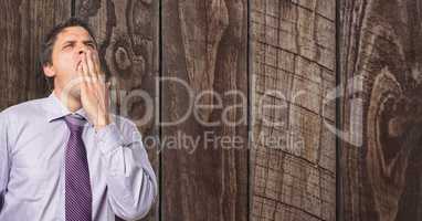 Tired businessman yawning against wooden wall