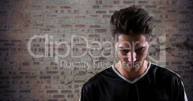 Soccer player looking down against brown brick wall