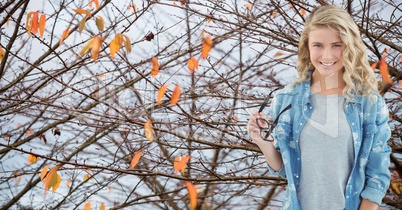 Portrait of smiling female hipster holding glasses while standing against trees