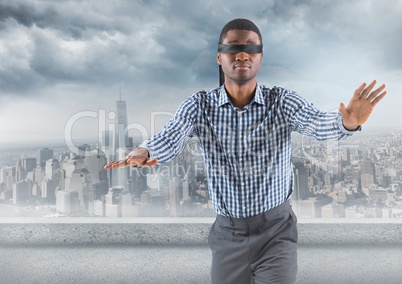 Business man blindfolded with against skyline with grey clouds