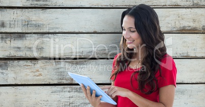 Smiling woman using digital tablet against wooden wall