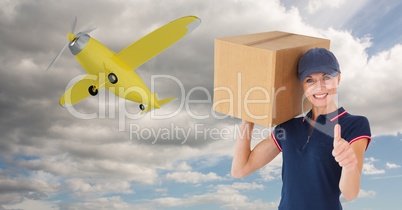 Delivery woman showing thumbs up while carrying parcel against airplane flying in sky