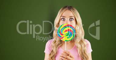 Portrait of shocked woman covering mouth with candy against green background