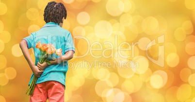 Rear view of boy hiding flowers behind back over bokeh