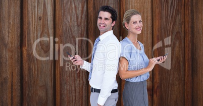 Smiling business people holding smart phone while standing back to back against wooden wall