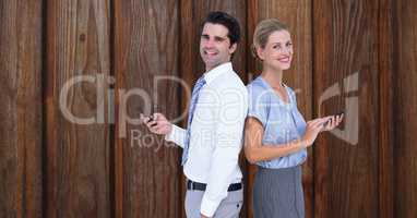 Smiling business people holding smart phone while standing back to back against wooden wall