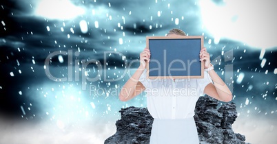 Woman covering face with slate while water splashing on rock