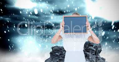 Woman covering face with slate while water splashing on rock