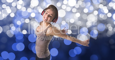 Happy woman dancing while listening to music on headphones against bokeh