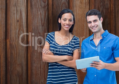 Portrait of confident couple with digital tablet against wooden wall
