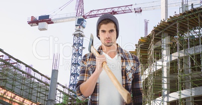 Hipster holding ax against incomplete buildings and crane