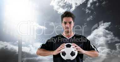 Confident player holding soccer ball against sky