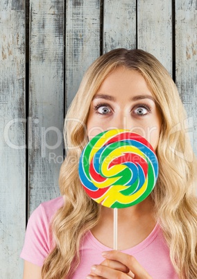 Portrait of shocked woman covering mouth with candy against wooden wall