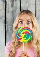 Portrait of shocked woman covering mouth with candy against wooden wall