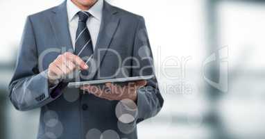 Business man mid section with tablet behind bokeh against blurry grey window