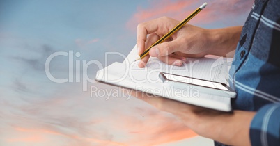 Midsection of businessman with mobile phone writing notes in book