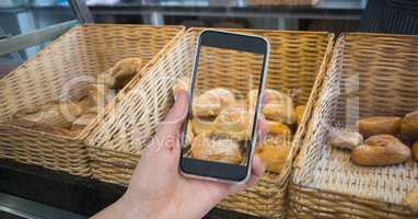 Hand photographing breads through smart phone in cafe