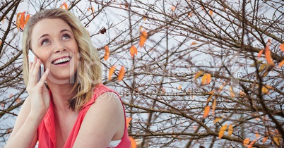 Smiling woman using mobile phone against autumn branches