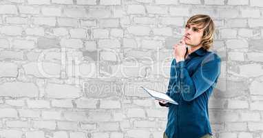Thoughtful hipster holding digital tablet against wall