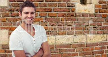 Young man with arms crossed smiling against brick wall