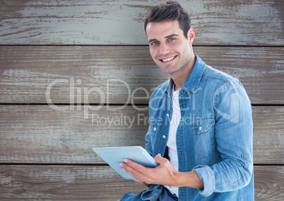 Portrait of smiling man holding digital tablet against wooden wall