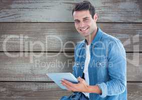 Portrait of smiling man holding digital tablet against wooden wall