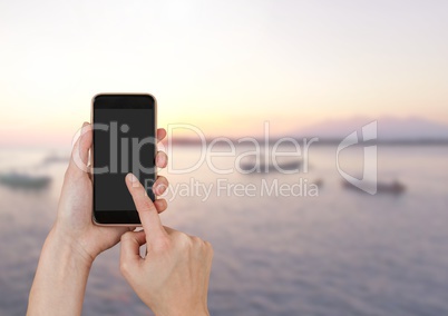 Hand Touching phone next to sea landscape