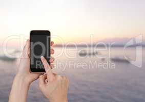 Hand Touching phone next to sea landscape