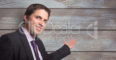 Portrait of smiling businessman gesturing towards wooden wall