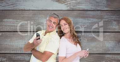Smiling couple using smart phone against wooden wall