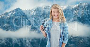 Smiling woman holding eyeglasses against snowcapped mountains
