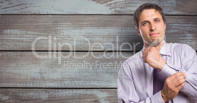 Portrait of confident businessman buttoning sleeve against wooden wall