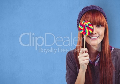 Happy female hipster covering eye with candy against blue background