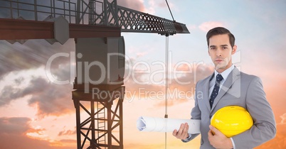 Architect holding hardhat and blueprint in front of crane