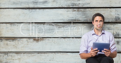 Confident businessman holding digital tablet while sitting against wooden wall