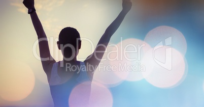Rear view of fit woman with arms raised by with bokeh