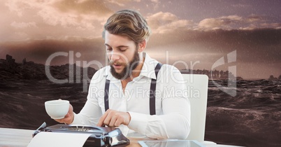 Male hipster using typewriter while holding coffee cup against sea