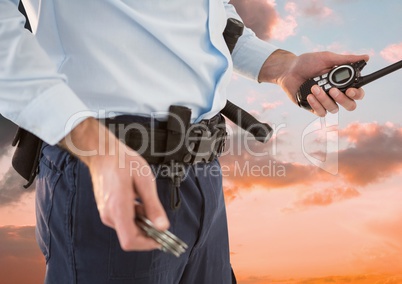Midsection of security guard holding roadio against sky during sunset