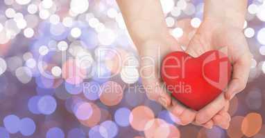 Close-up of female's hands holding heart shape over glowing bokeh