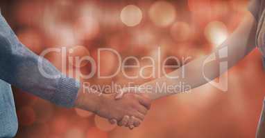 Midsection of couple shaking hands against bokeh