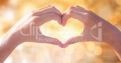 Cropped image of couple making heart shape with hands against bokeh
