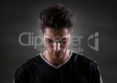 Soccer player looking down against grey wall and flare