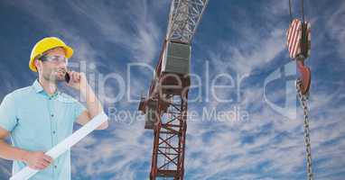 Architect using mobile phone while holding blue print by crane against sky