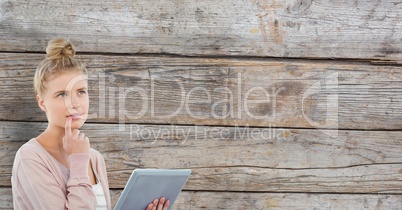 Thoughtful woman holding digital tablet against wooden wall