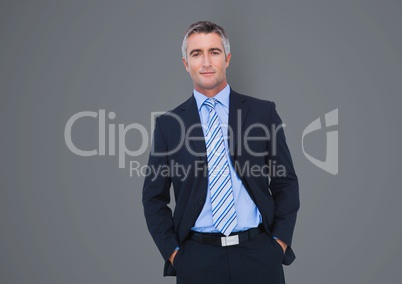 Confident businessman with hands in pockets over gray background