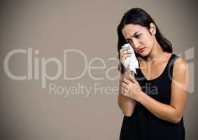 Woman crying into tissue against brown background